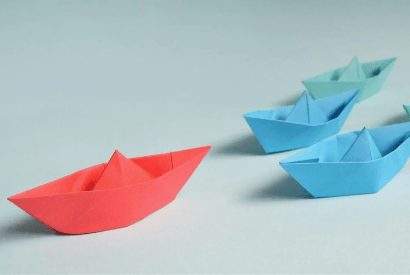 A red sailboat followed by blue sailboats. 