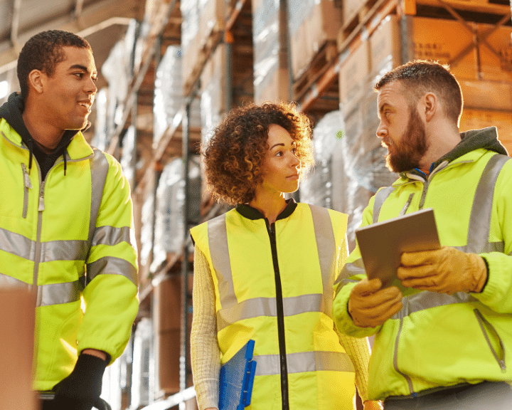 woman and two men supply chain executives work in warehouse to send and receive bookings, ISF details, attachments, and invoices from shipper customers.